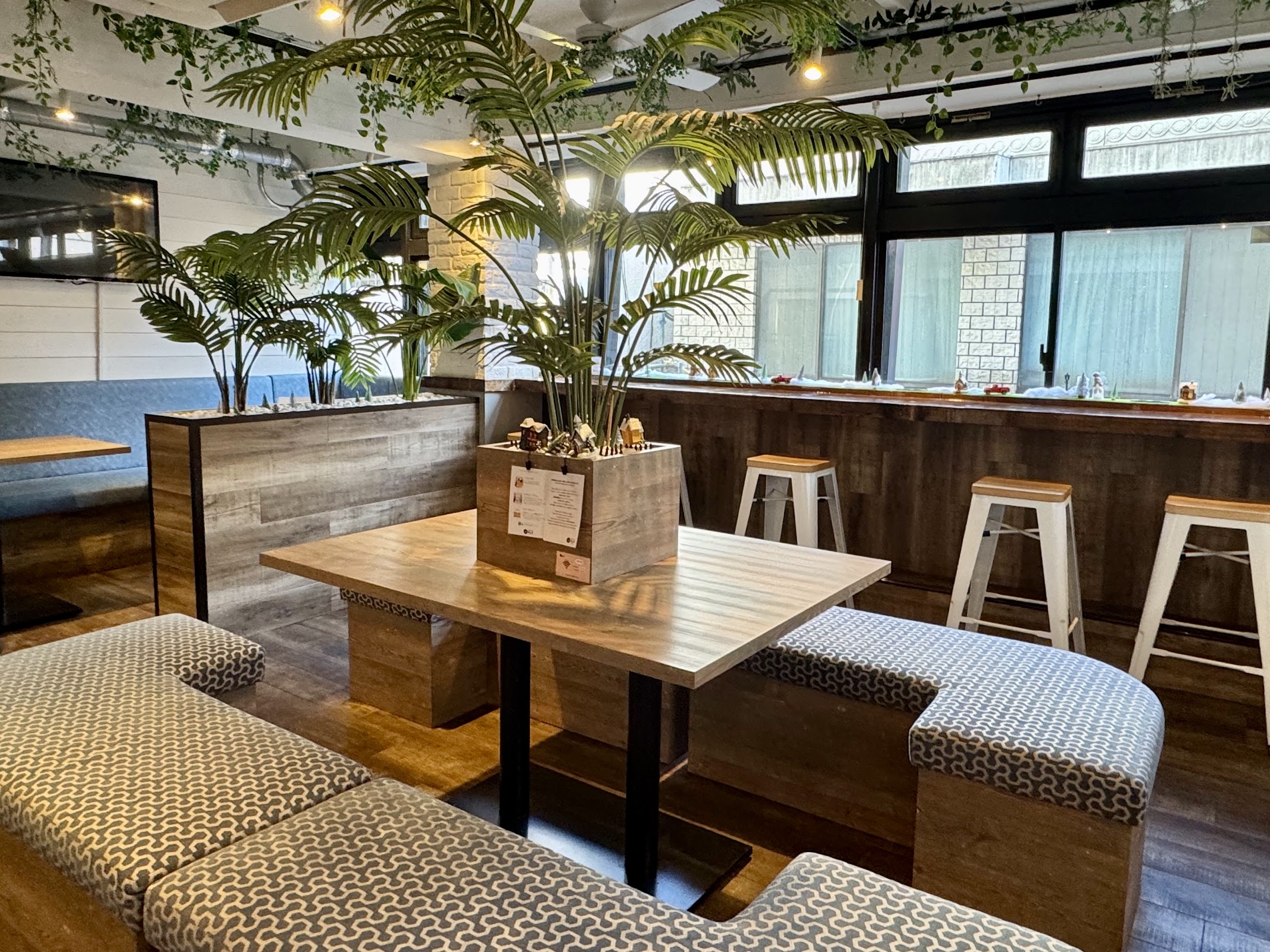 木目テーブルにノートパソコンと観葉植物、自然光に照らされた店内の作業席