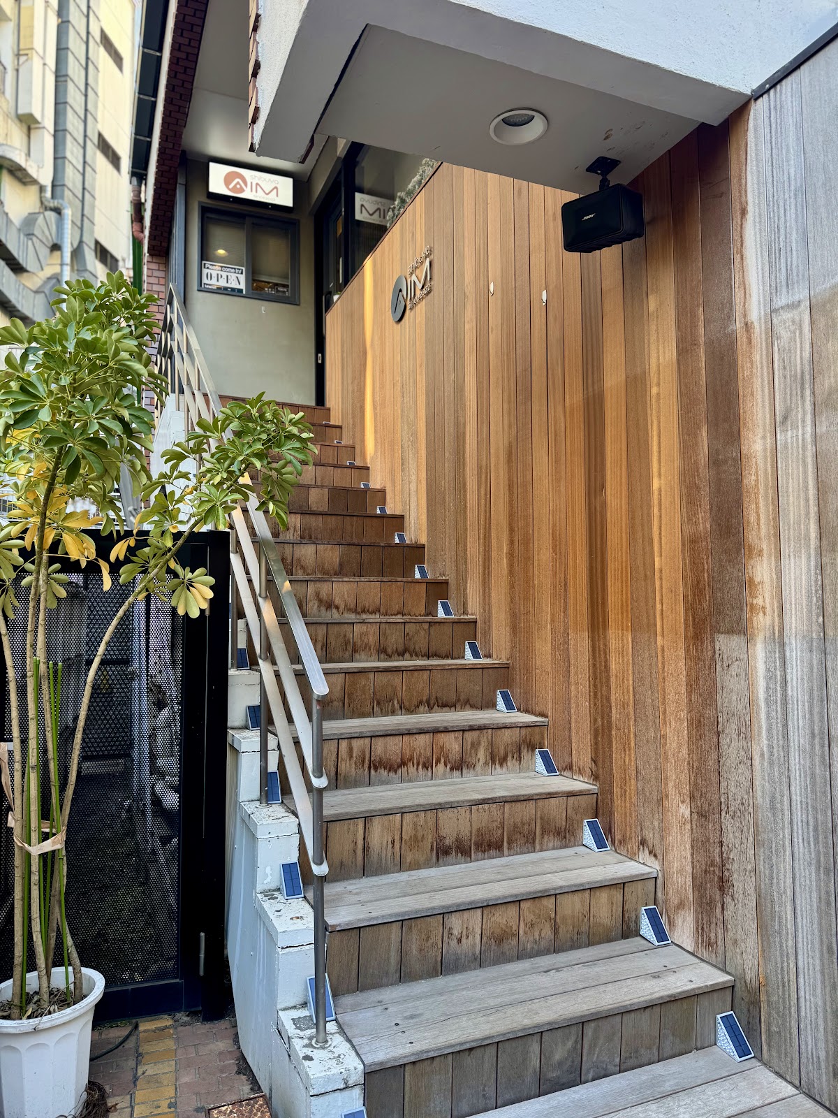 階段途中の「AIM」「OPEN」看板、木材壁と入口扉